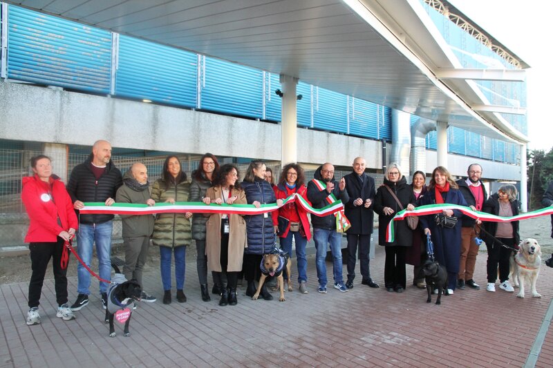 gruppo di persone che tagliano un nastro tricolore di fronte all'aeroporto, inaugurando l'area per cani da assistenza